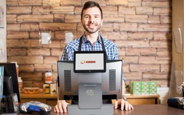 a retail employee smiles as he stands behind a counter with a KORONA POS system