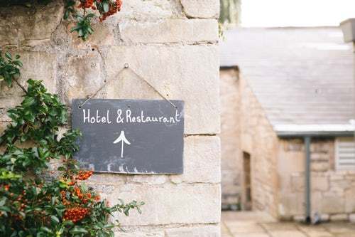 a sign for a hotel and restaurant hangs outside on an old stone street
