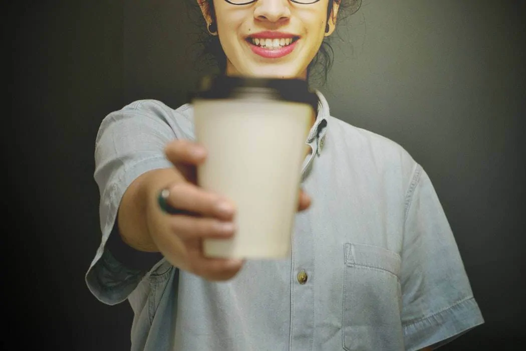 a barista offers a coffee in a paper cup
