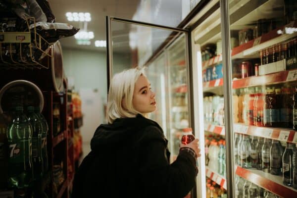 a convenience store shopper selects a drink from a refrigerator