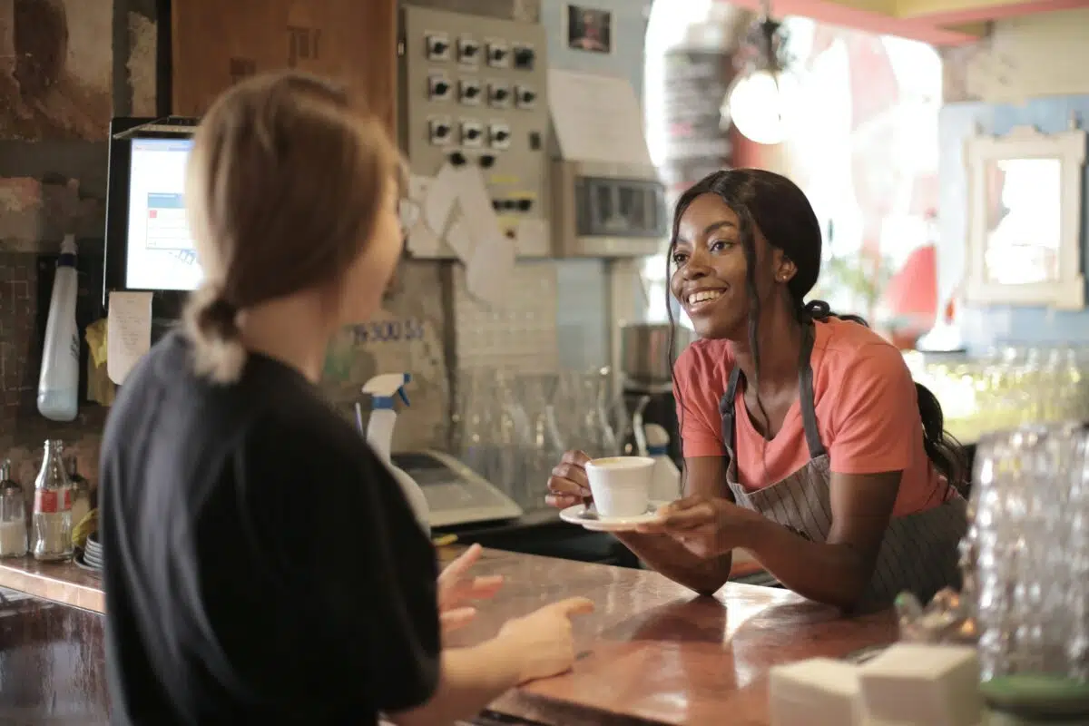 a barista smiles as they serve a coffee shop customer