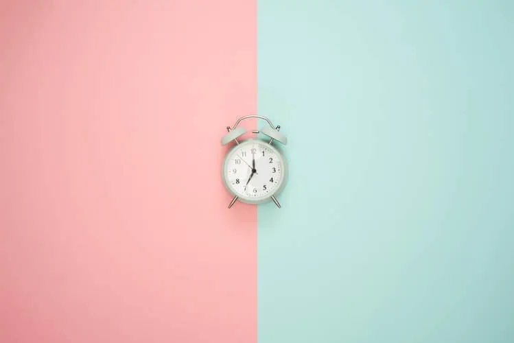 an old fashioned alarm clock on a pastel pink and blue background