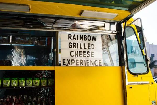a QSR yellow food truck with a sign that reads 'rainbow grilled cheese experience'