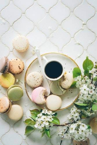 macaroons and black coffee sit on a plate on top of a tile background with flowers
