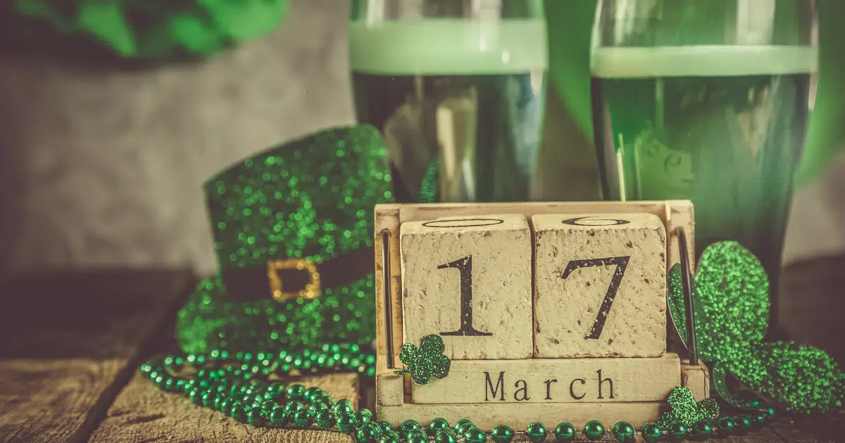 a wood block reading '17 March' sits in front of a St. Patrick's day hat, beads, and a couple of beers