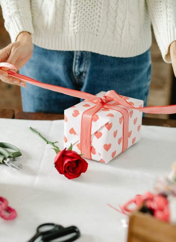 a retail store owner wraps a valentine's day gift box for a customer on a table with roses