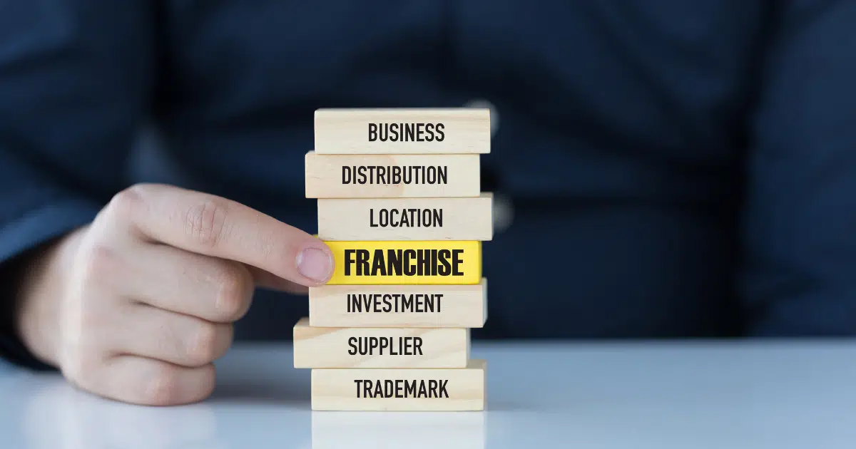a finger points to the word 'franchise'  on a wood block in a stack of other wood blocks with different retail business related terms written on them