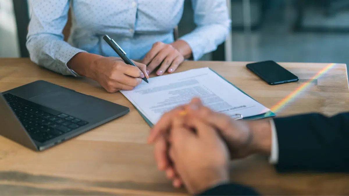 a retail operator sits at a desk and signs a contract while sitting across from another person 