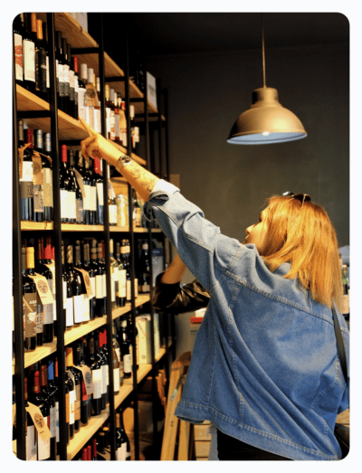 a woman in a liquor store selects a bottle of wine from a shelf