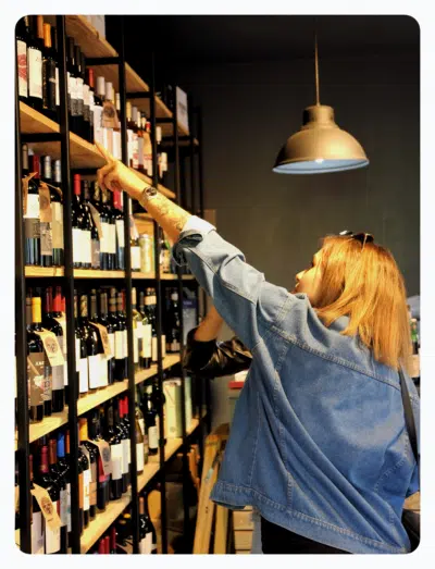 a liquor store customer points at wine bottles on shelves