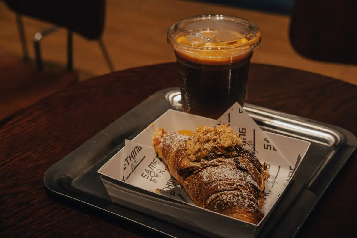 a croissant and a cold brew sit on a tray  at a table in a coffee shop