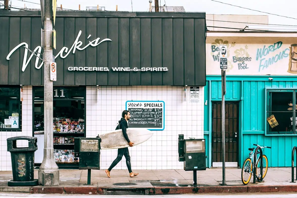 a surfer walks past a liquor store in California