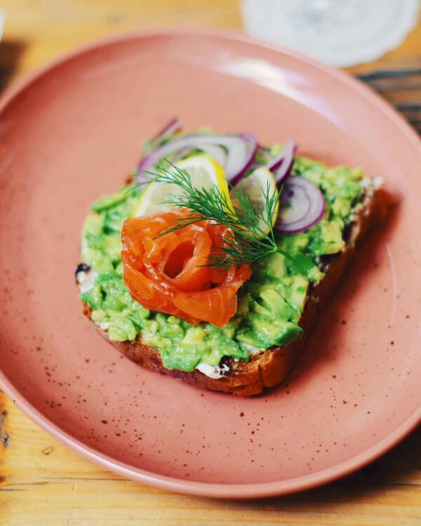a photo in a coffee shop of avocado toast topped with smoked salmon, onions, and herbs