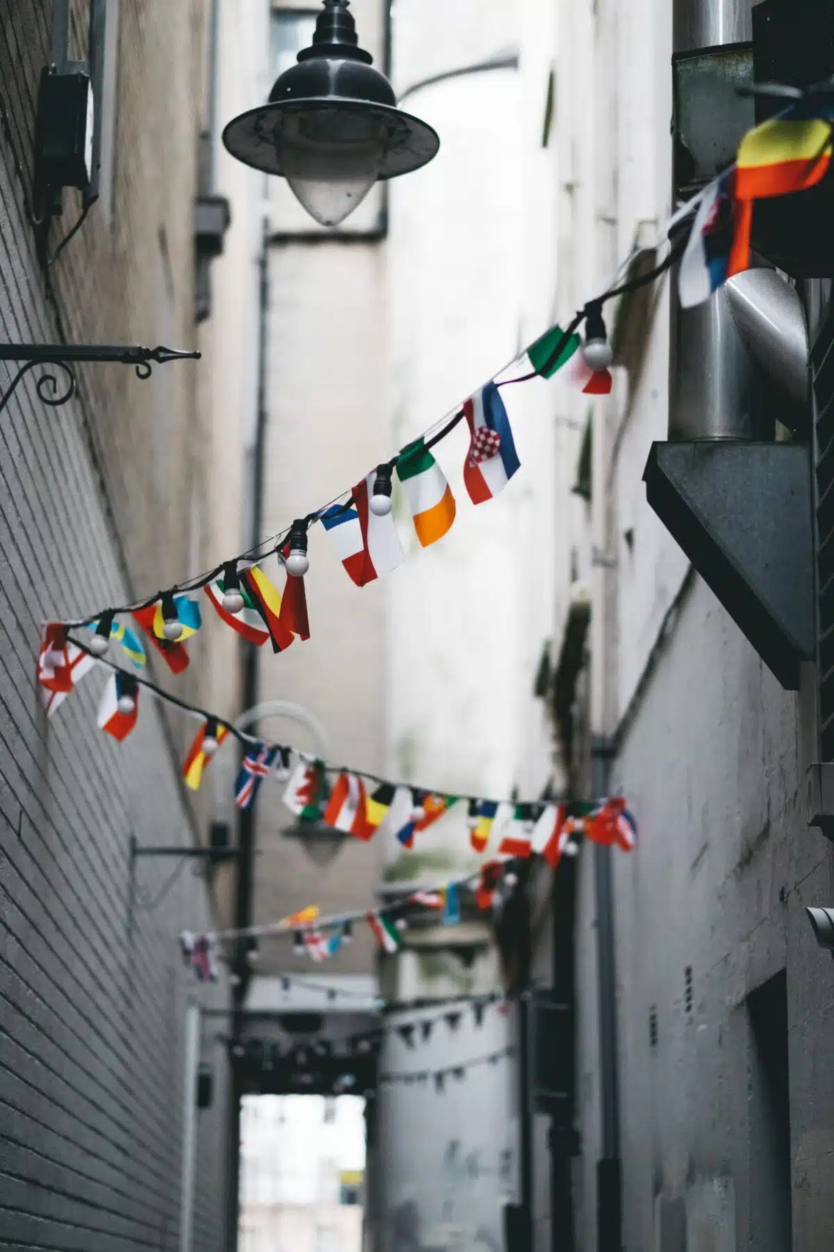 An alley in a city with small country flags strung between either side of it