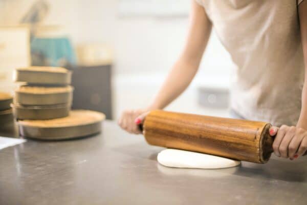 a baker uses a rolling pin to roll out dough next to some tarts in tart tins