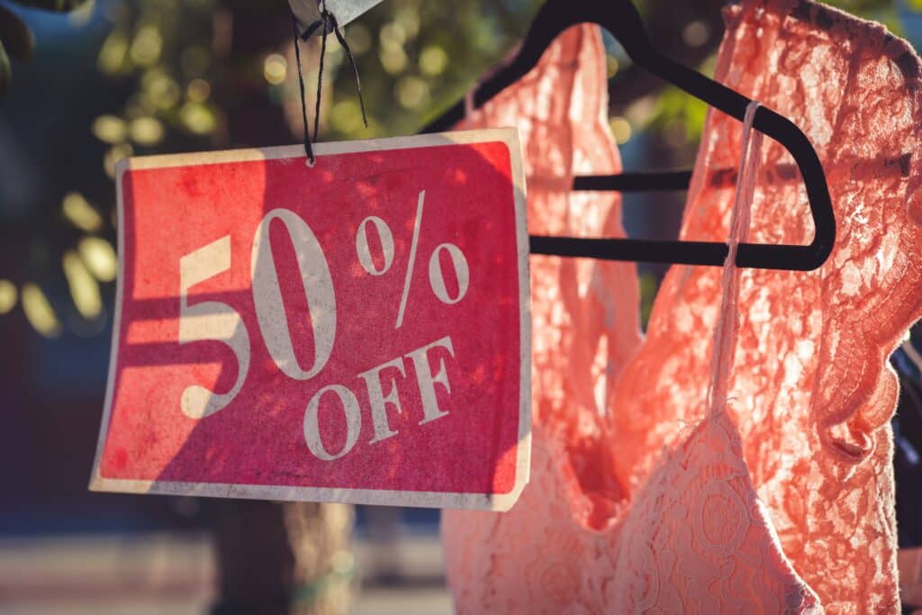 a retail promotion discount sign hangs in front of a pink dress on a clothing rack