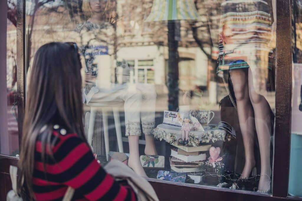 a window shopper looks at clothing outside a retail store