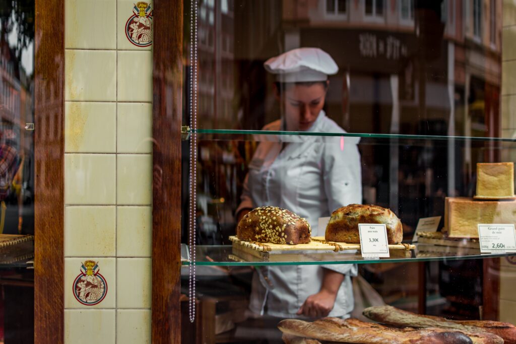 exterior of a bakery window with a chef looking over loaves and baguettes
