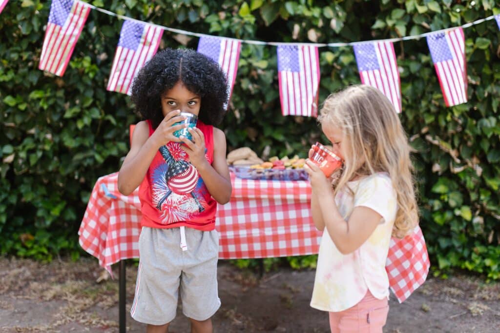 children sip drinks at a 4th of July barbecue with American flags in the background