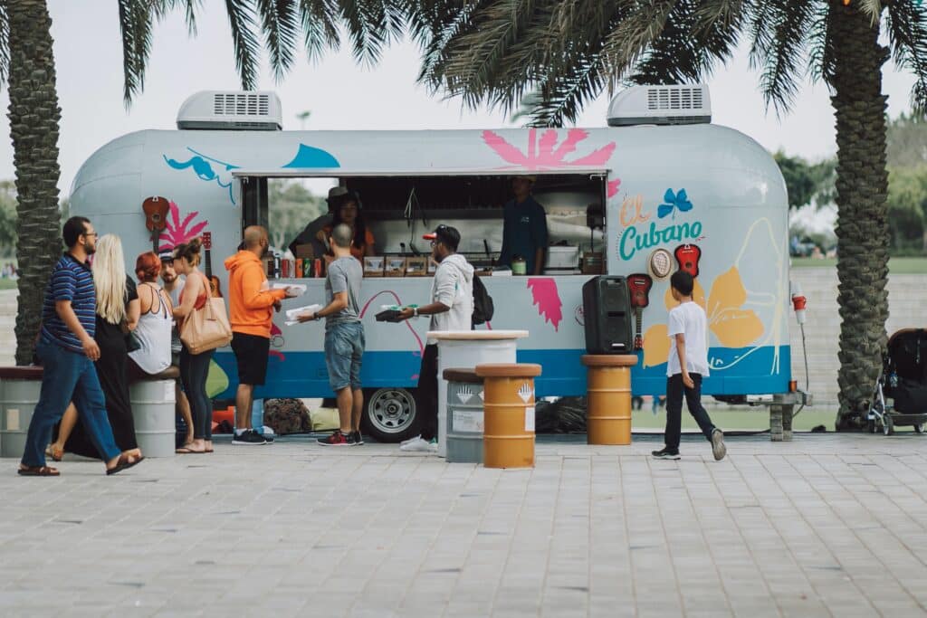 a food truck under palm trees with customers standing in front