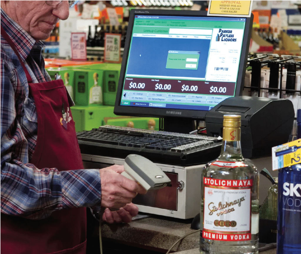 Cashier scans a bottle of vodka at a liquor store checkout area with a liquor POS system next to him