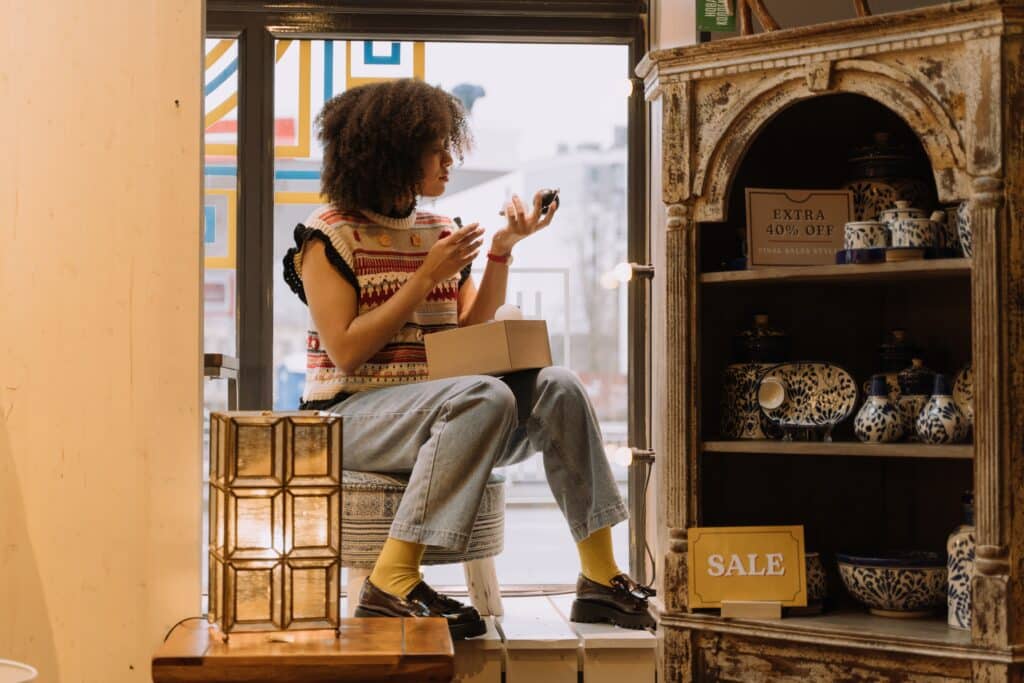 A retail employee sits on a chair while setting up a window display in a gift shop