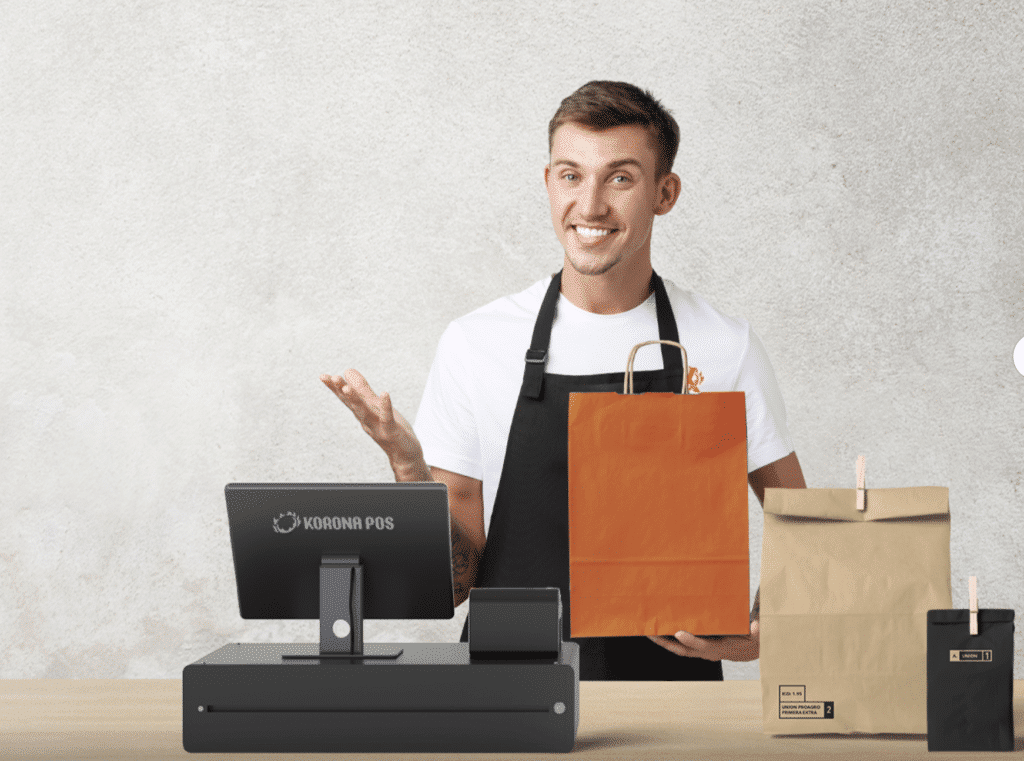 Cashier stands behind a KORONA POS checkout terminal at a winery retail shop. He's holding a bag and preparing to hand it to a customer behind the camera.