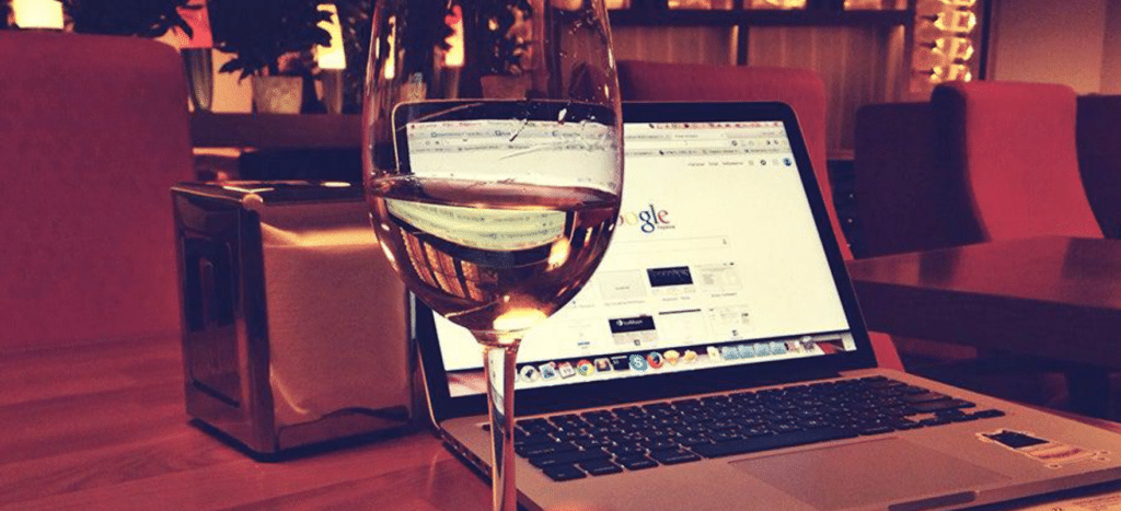 A person drinks a glass of wine while working on their laptop to set up their winery business to sell products online