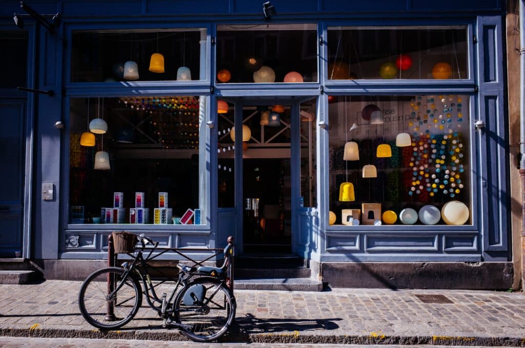 exterior window of a blue retail store with lots of hanging lamps and a cobblestone street and bicycle outside