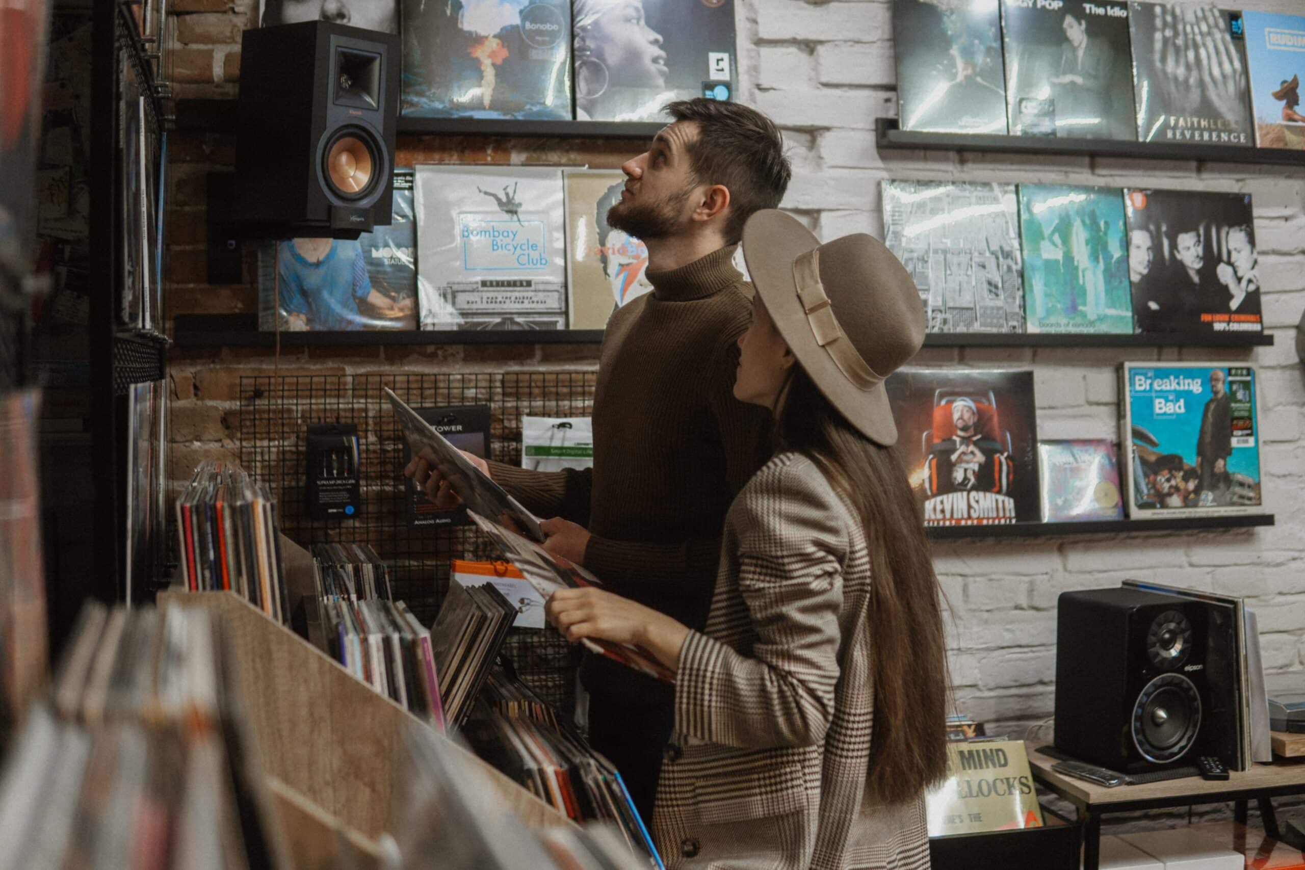 two shoppers in a record store hold albums while they look up at the wall