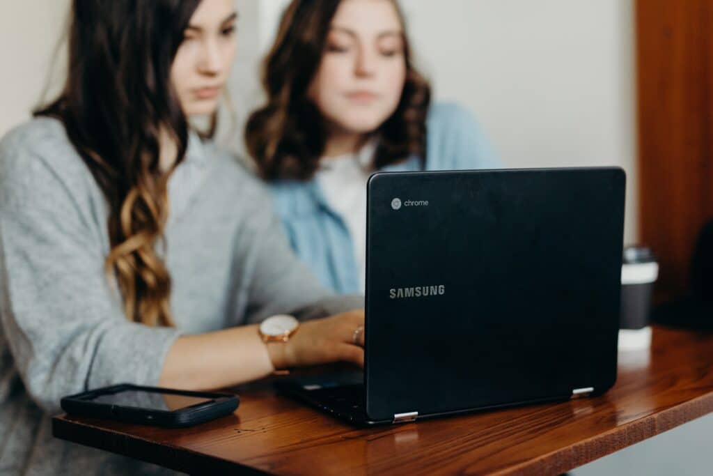 two retail shop owners sit at a table and write a business plan on a laptop