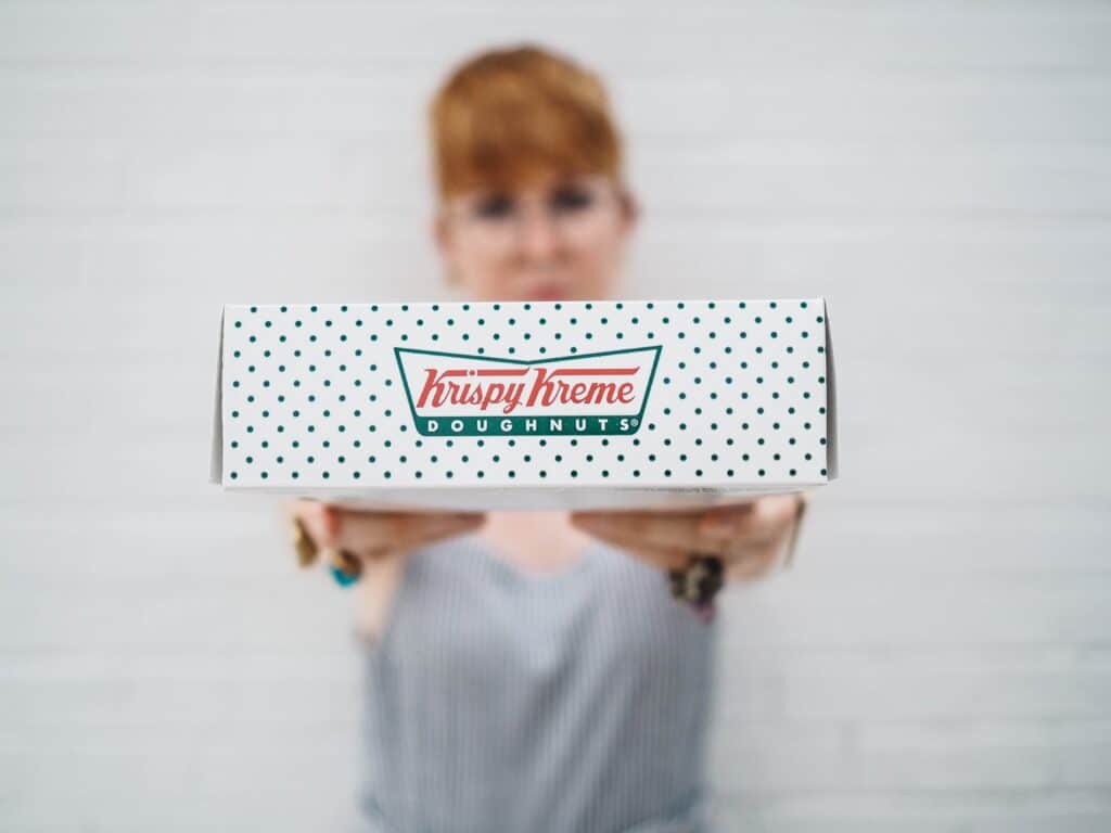 a person holds a krispy kreme doughnuts box up to the camera