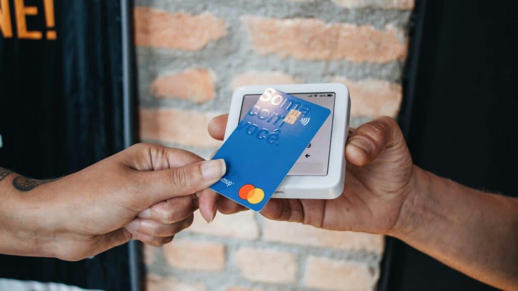 a person holds their credit card to a mobile card reader tap & pay payment terminal that a different person is holding