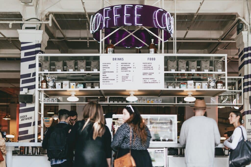 People wait in line at a small coffee shop in a market area